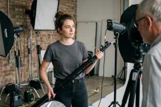 Jeune assistante photographe tenant un réflecteur dans un studio professionnel, observant le travail du photographe principal